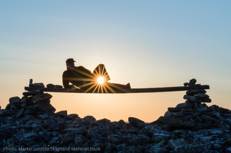 A silhouette of a person reclining on a bench against a setting sun