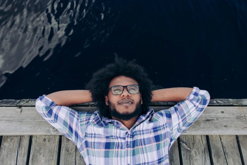 A student relaxing on his back, by a lake shore